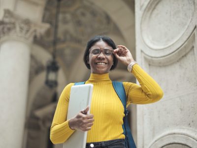 young woman at the entrance of a school holding a computer young woman at the entrance of a school holding a computer