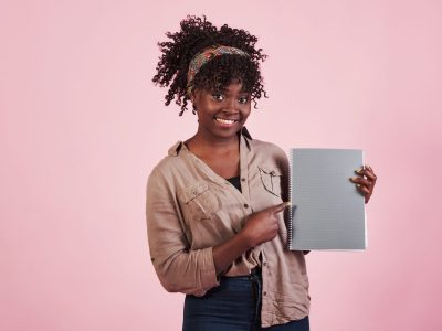 Woman holding grey notepad in her hands at pink studio background Woman holding grey notepad in her hands at pink studio background.